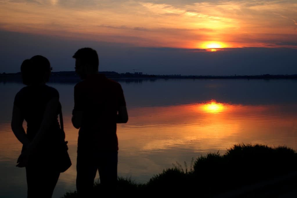 夕暮れの湖畔に寄り添って未来を見つめるふたりのシルエット
