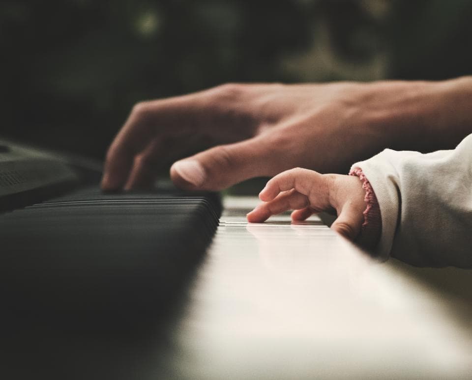 大人の手にそっと導かれ、はじめて鍵盤に触れる子どもの手